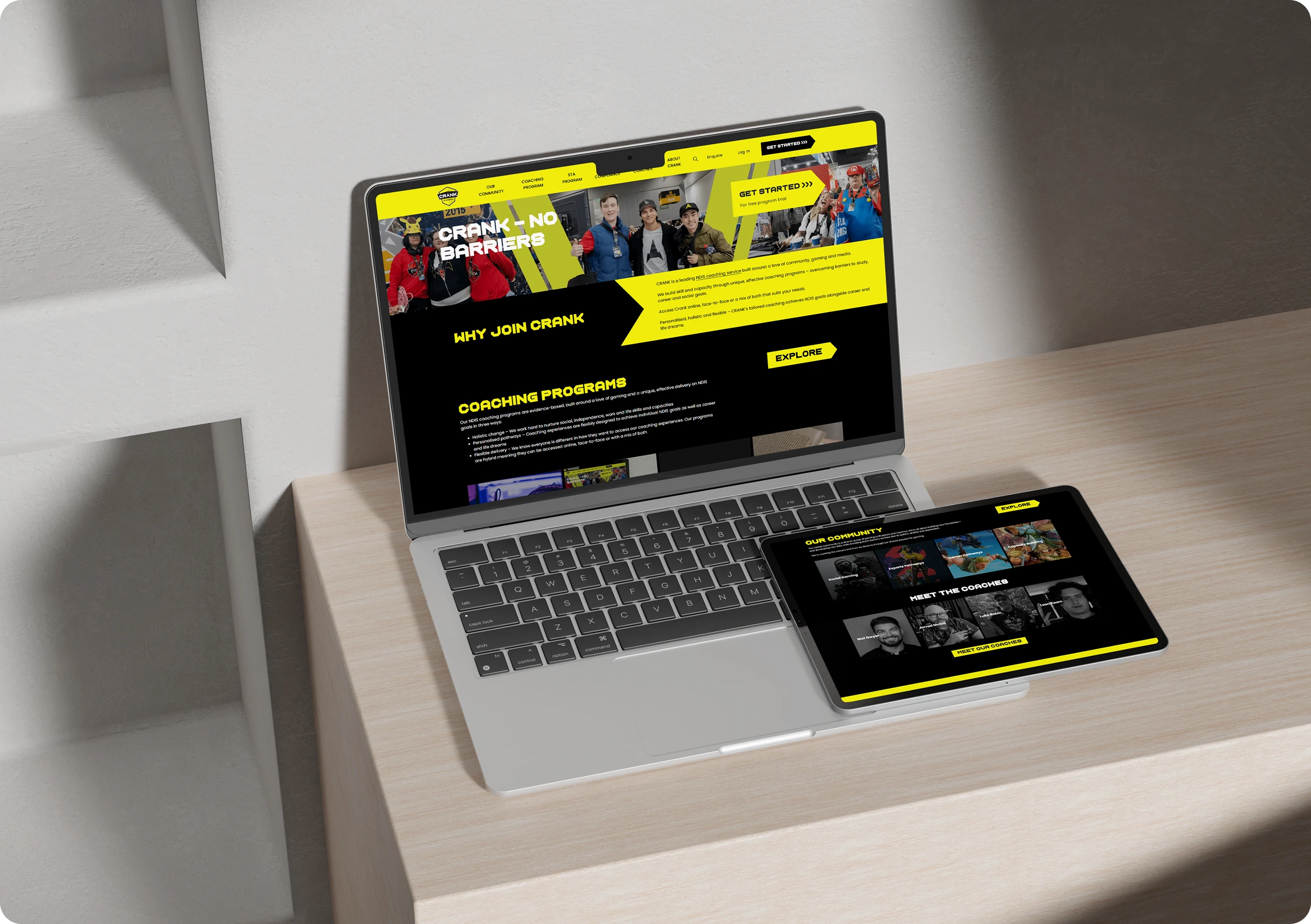 A laptop and tablet on a light wooden desk display the same sports-themed website with a black and yellow color scheme.