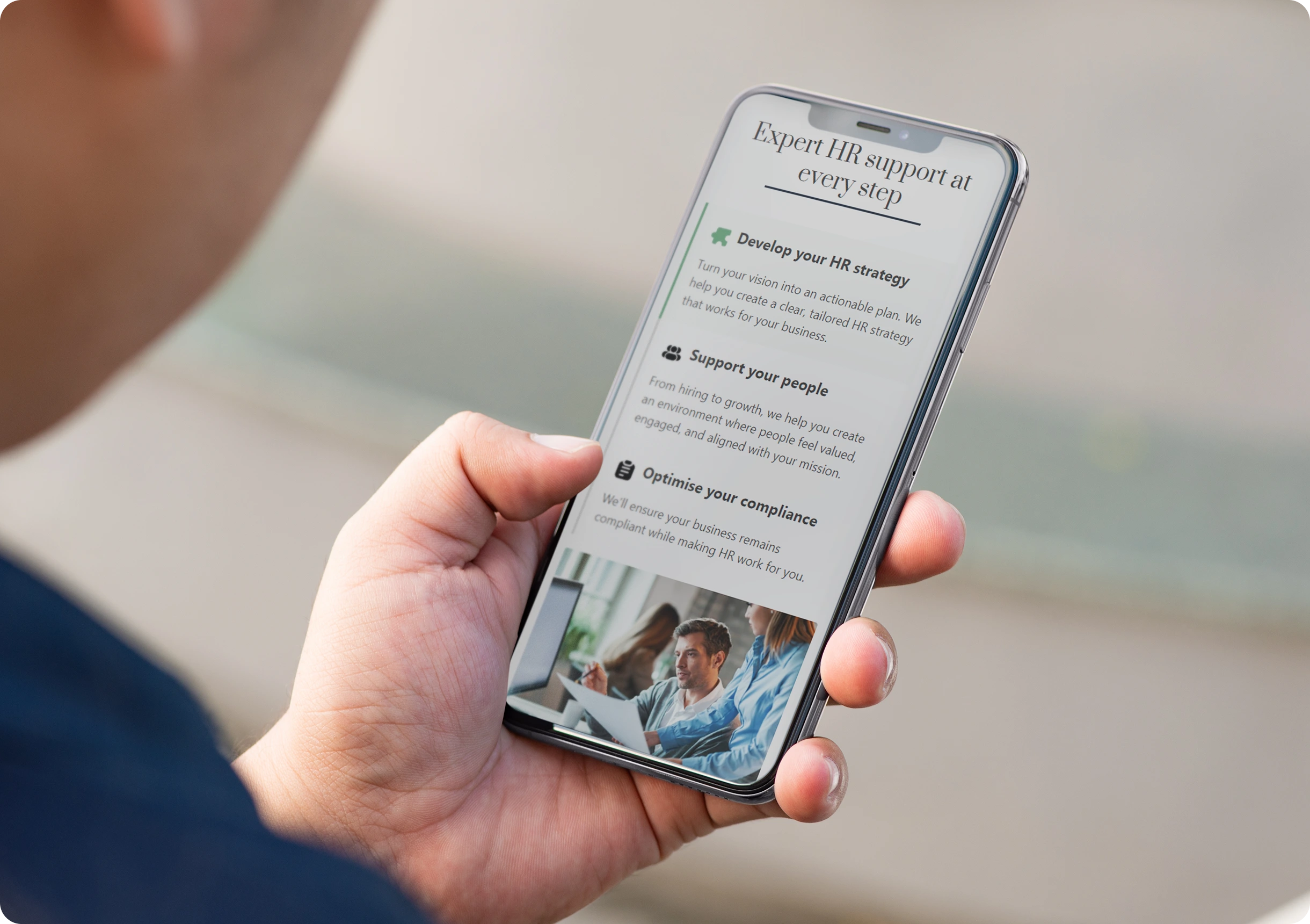 A person holds a smartphone displaying an HR support webpage with sections about strategy, supporting people, and compliance.