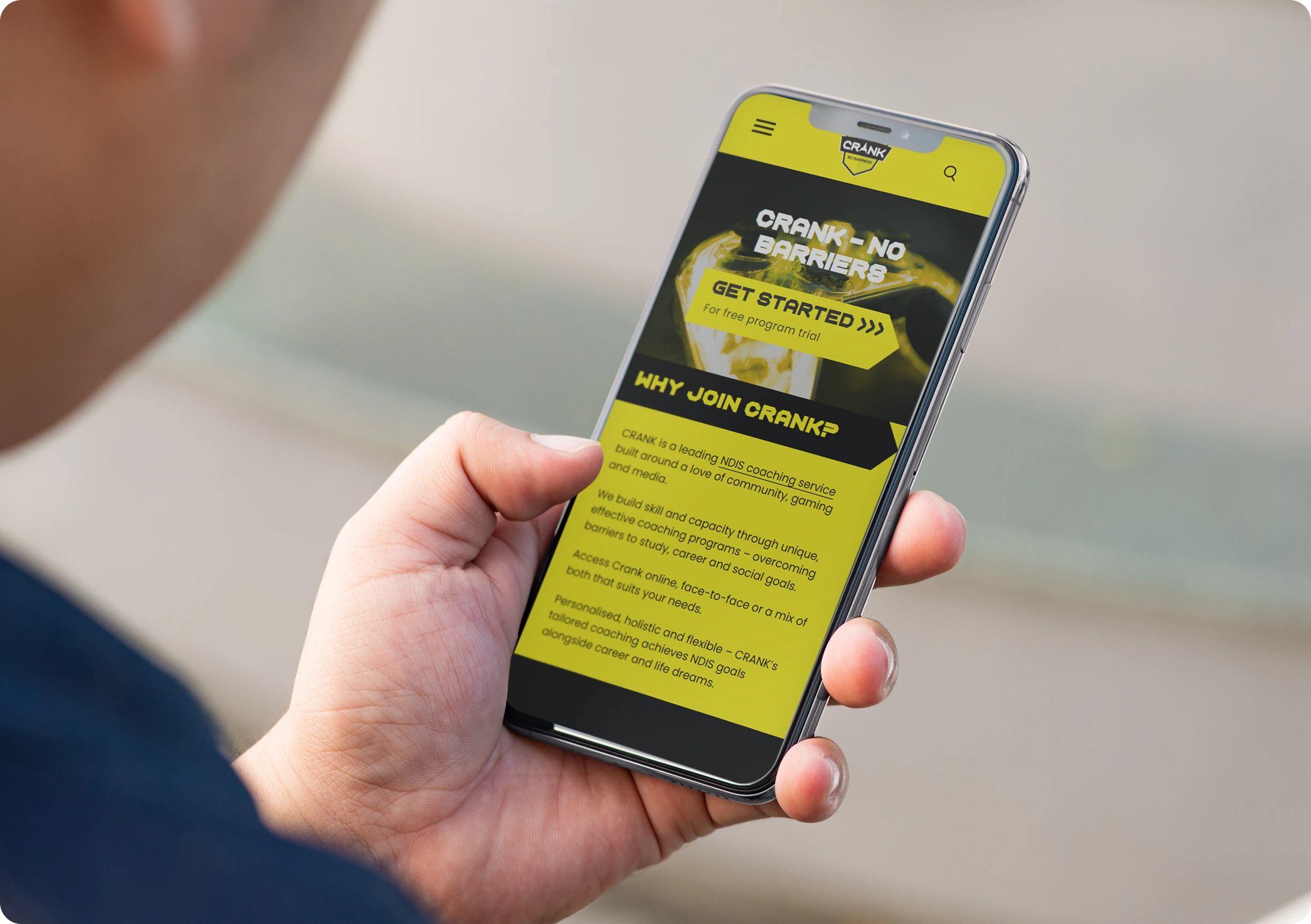 Person holding a smartphone displaying a website with yellow and black text promoting a program called CRANK, highlighting benefits and a call-to-action to get started.