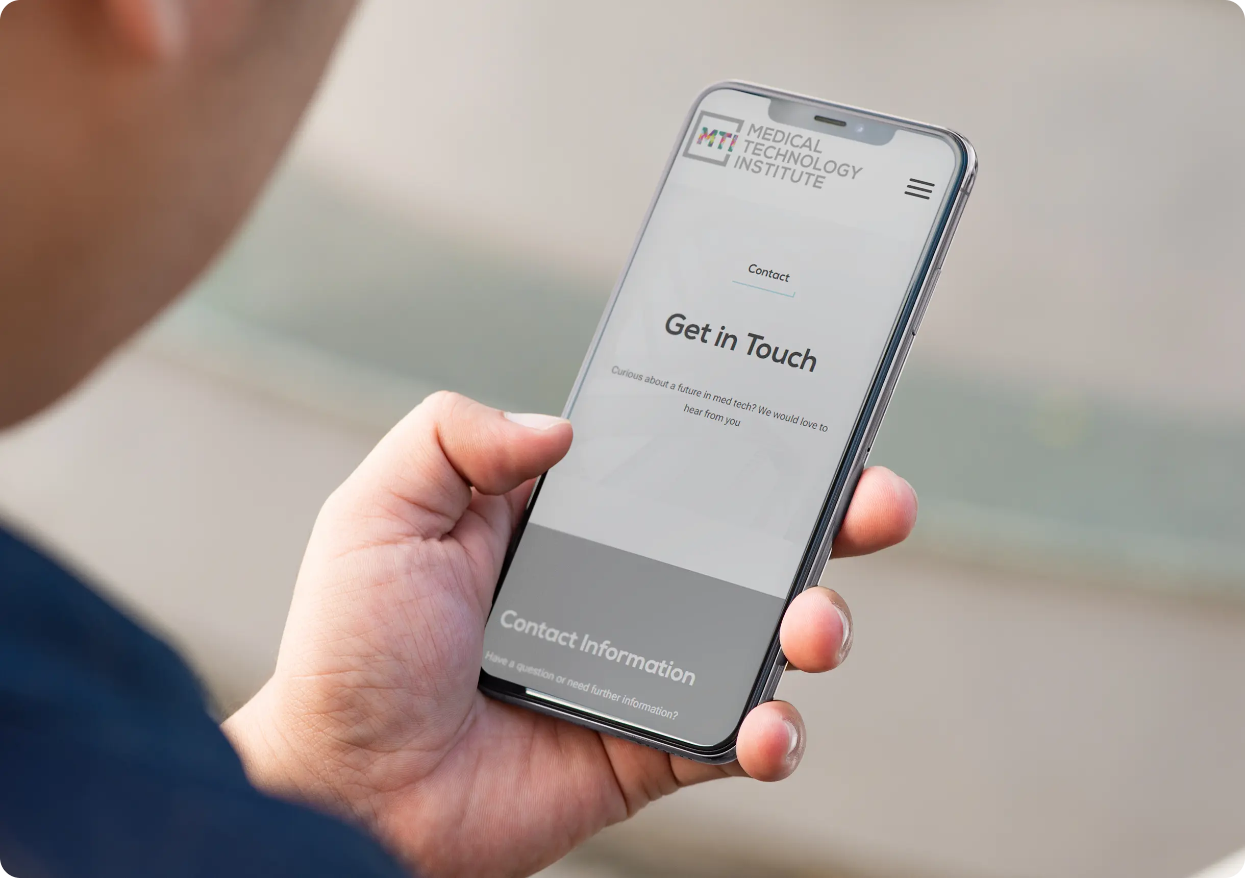 A person holds a smartphone displaying the Get in Touch contact page of the Medical Technology Institute website.