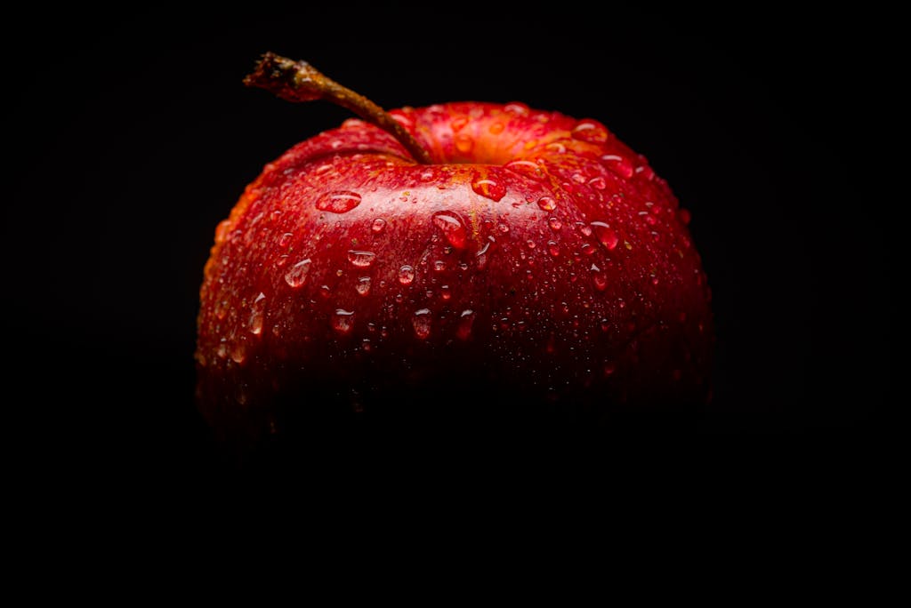 Close-up of a fresh red apple with water droplets against a dark background.