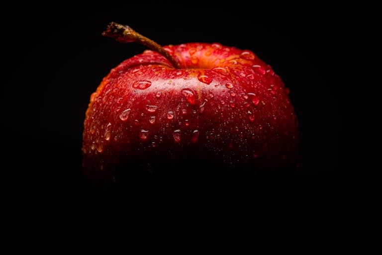 Close-up of a fresh red apple with water droplets against a dark background.